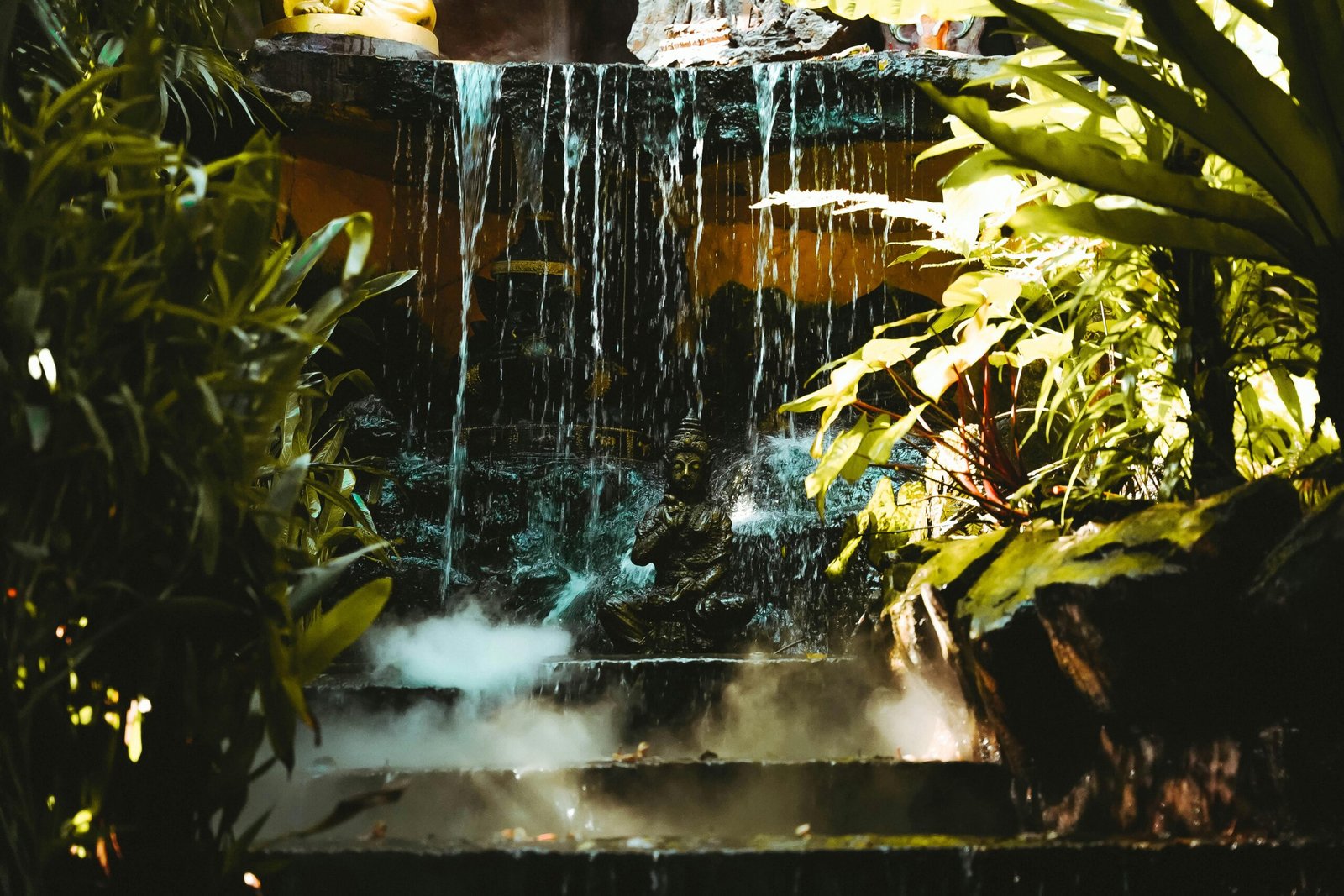 A serene Buddha statue surrounded by lush foliage and a cascading waterfall in Bangkok, Thailand.